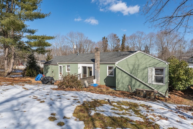 snow covered property featuring a shingled roof and a chimney