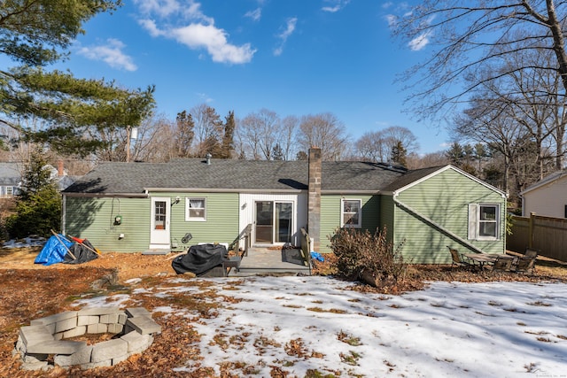 snow covered house with a chimney, fence, and a fire pit