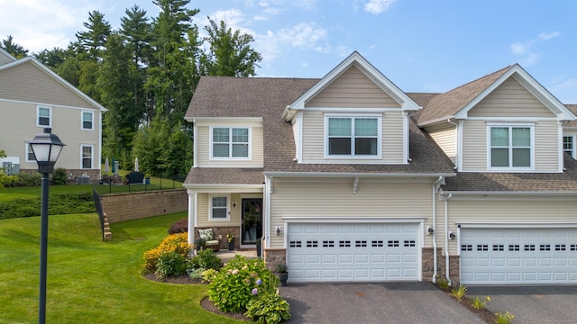 view of front of home with an attached garage, roof with shingles, driveway, and a front lawn