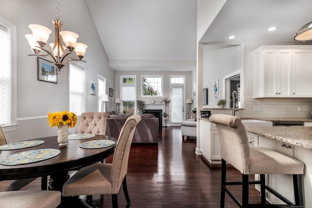 dining area featuring dark wood-style floors, vaulted ceiling, a fireplace, a notable chandelier, and recessed lighting