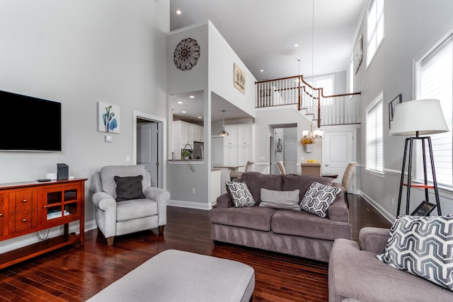 living area with dark wood-style floors, recessed lighting, a towering ceiling, an inviting chandelier, and baseboards