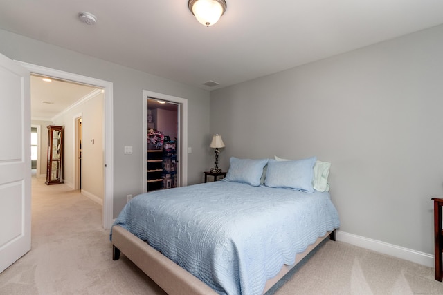 bedroom with light carpet, baseboards, and a walk in closet