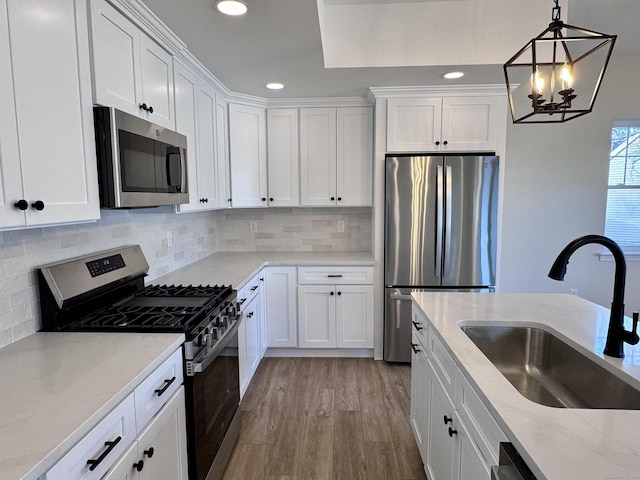 kitchen with tasteful backsplash, appliances with stainless steel finishes, light wood-style floors, white cabinets, and a sink