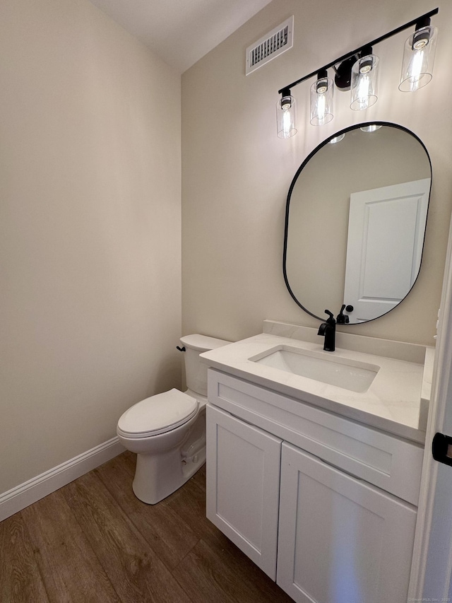 bathroom featuring baseboards, visible vents, toilet, wood finished floors, and vanity