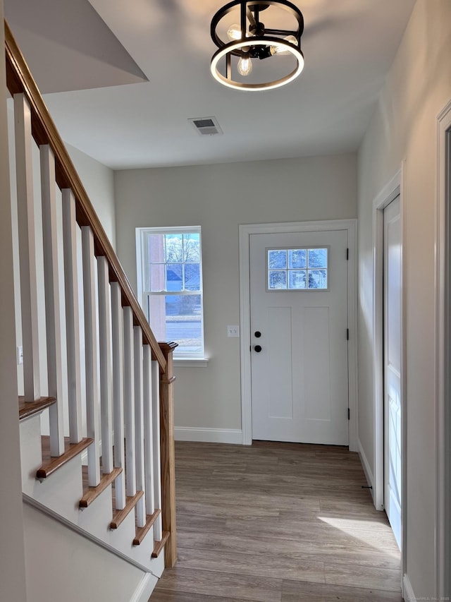 foyer featuring stairs, visible vents, baseboards, and wood finished floors