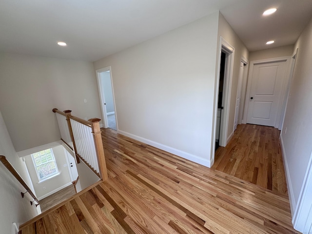 corridor featuring light wood finished floors, recessed lighting, an upstairs landing, and baseboards