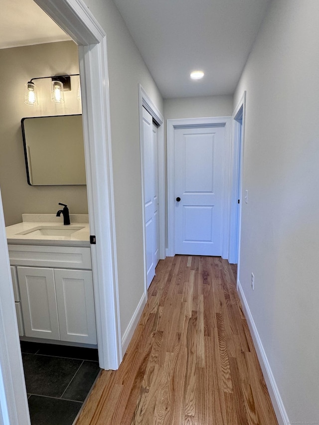 corridor featuring baseboards, a sink, and wood finished floors