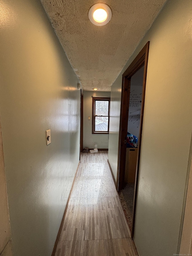 corridor with a textured ceiling, wood finished floors, and baseboards