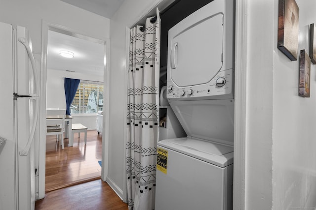 clothes washing area with laundry area, baseboards, wood finished floors, and stacked washer and clothes dryer