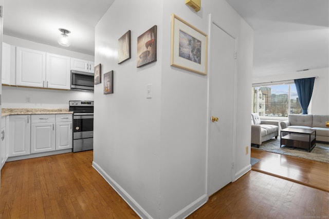 kitchen with stainless steel appliances, white cabinetry, baseboards, open floor plan, and hardwood / wood-style floors