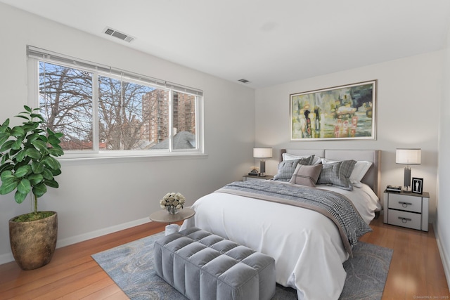 bedroom with wood finished floors, visible vents, and baseboards