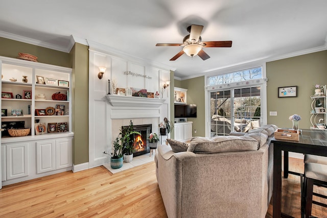 living room with a fireplace, crown molding, light wood-style flooring, ceiling fan, and baseboards