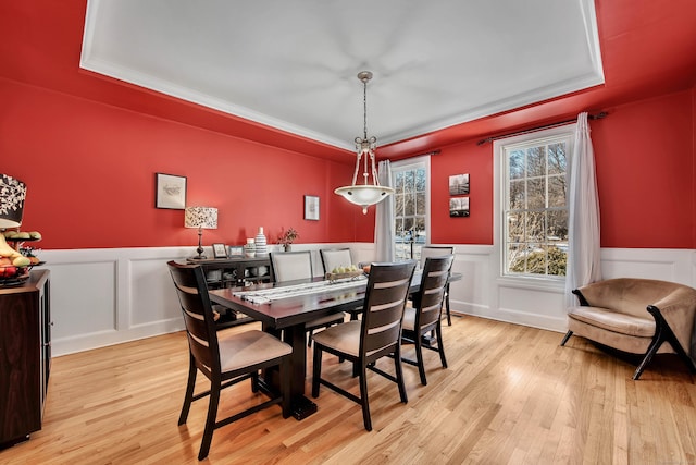 dining area featuring wainscoting, a raised ceiling, and light wood-style floors