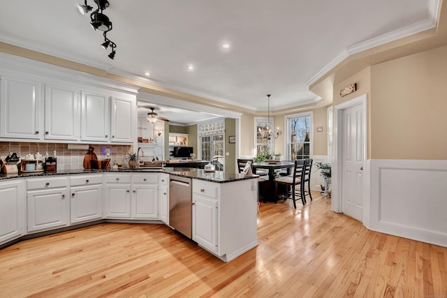 kitchen with stainless steel dishwasher, white cabinetry, light wood-type flooring, dark stone counters, and a peninsula