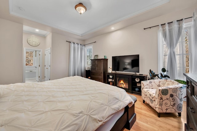 bedroom featuring a raised ceiling, ensuite bath, crown molding, light wood-style floors, and recessed lighting