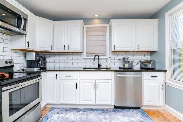 kitchen featuring backsplash, appliances with stainless steel finishes, white cabinets, a sink, and light wood-type flooring