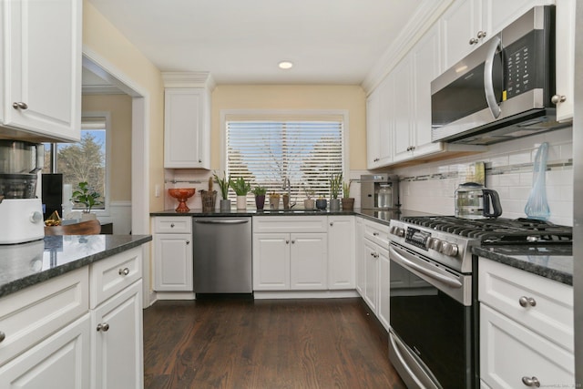 kitchen with white cabinets, appliances with stainless steel finishes, dark wood-type flooring, a sink, and backsplash