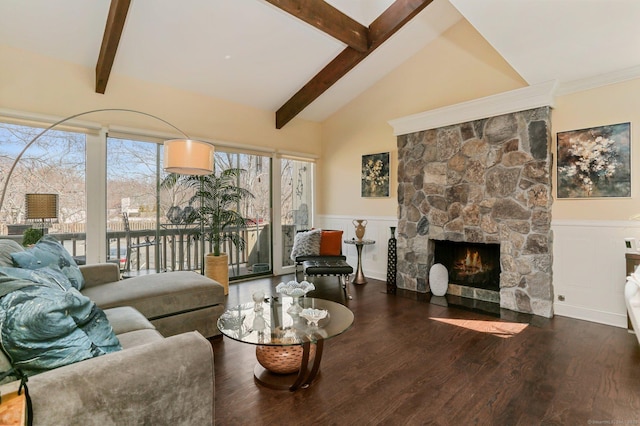 living area with beam ceiling, wainscoting, a stone fireplace, and wood finished floors