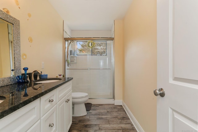 bathroom with toilet, a sink, a shower stall, wood tiled floor, and double vanity