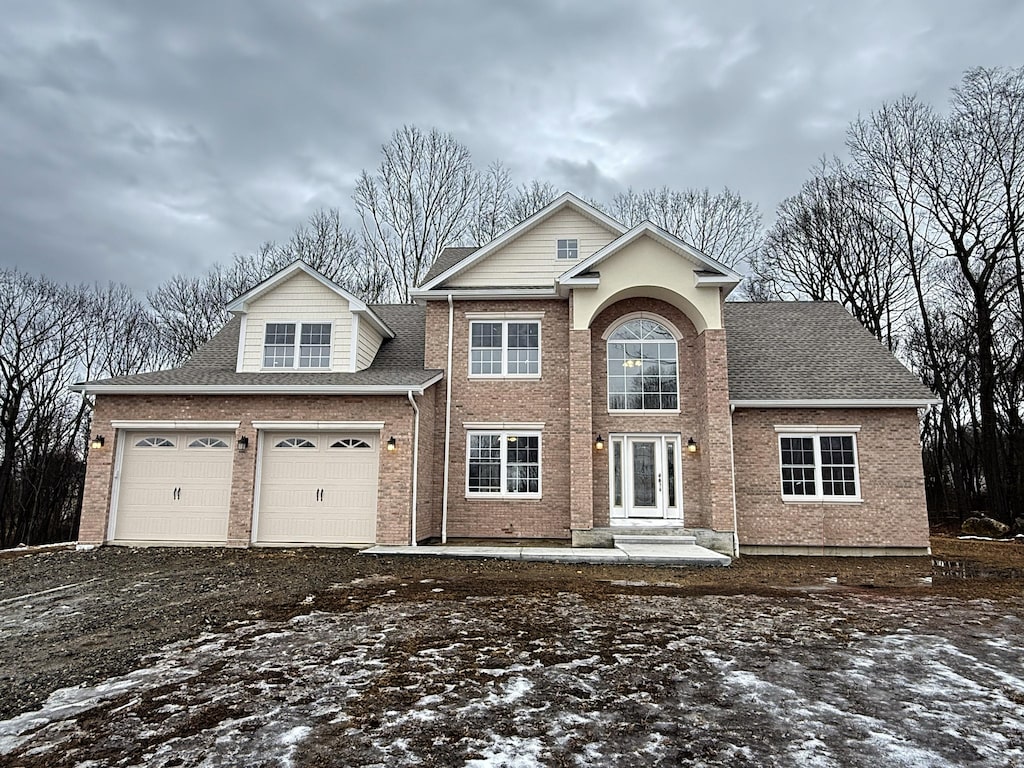 traditional home featuring a garage, roof with shingles, and brick siding