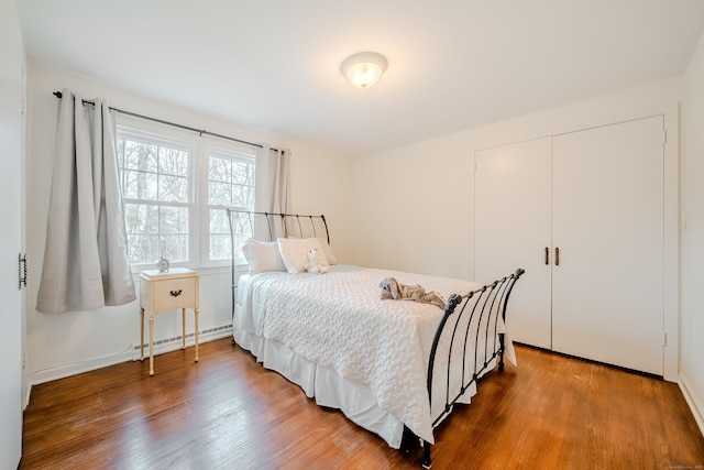 bedroom with a closet, baseboard heating, and wood finished floors