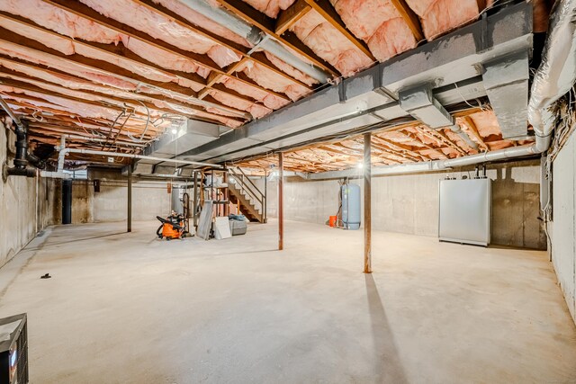 unfinished below grade area featuring water heater, stairs, and refrigerator