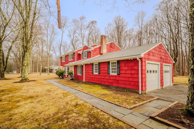 view of side of property featuring a detached garage, a chimney, a lawn, and roof with shingles