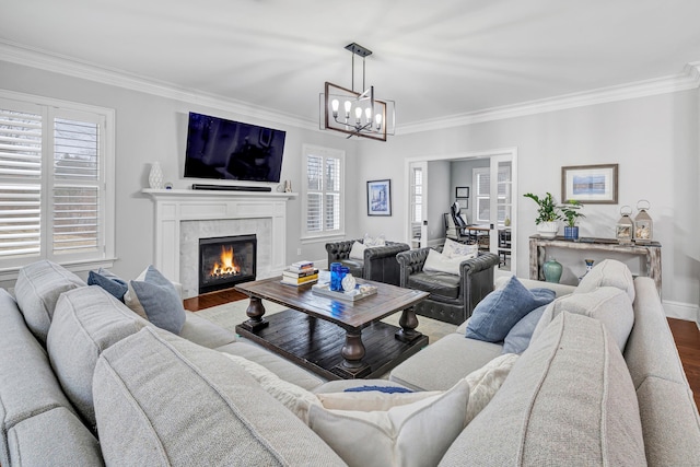 living room featuring a tiled fireplace, an inviting chandelier, ornamental molding, wood finished floors, and baseboards