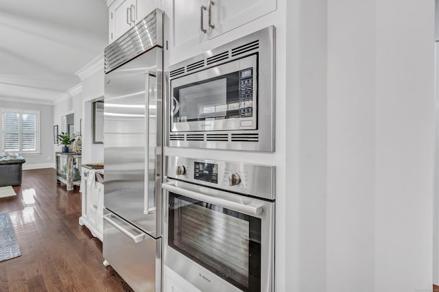 kitchen featuring built in appliances, dark wood-style flooring, white cabinetry, baseboards, and crown molding