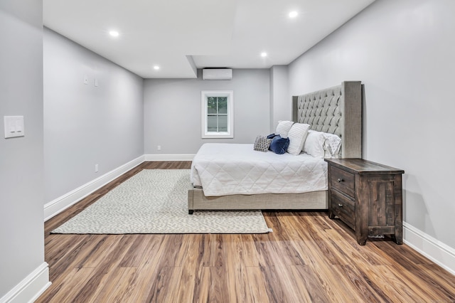 bedroom with wood finished floors, baseboards, and a wall mounted AC