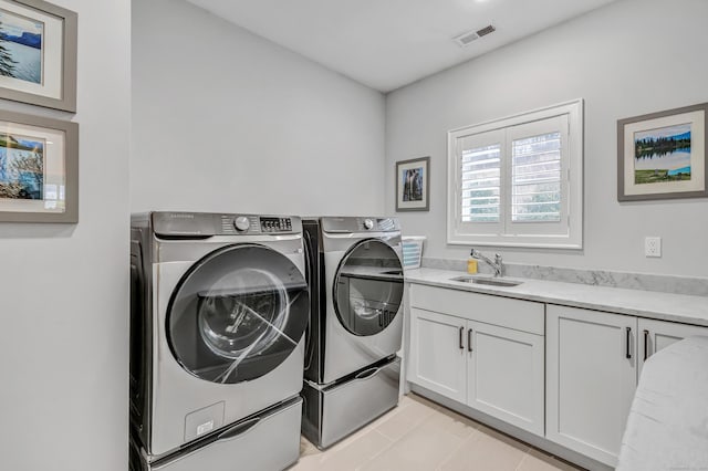 clothes washing area with light tile patterned floors, cabinet space, visible vents, washer and dryer, and a sink