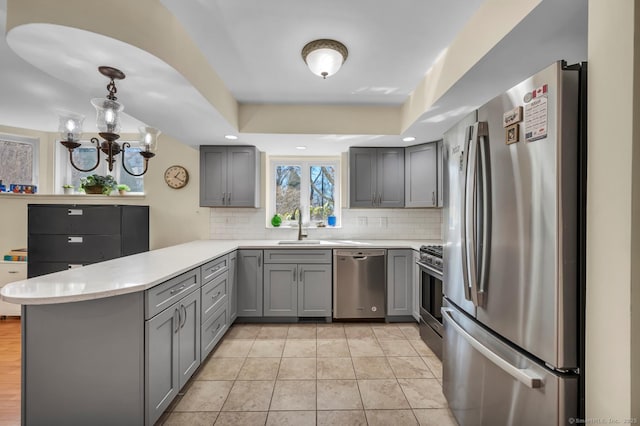 kitchen featuring gray cabinets, a sink, appliances with stainless steel finishes, a peninsula, and light countertops