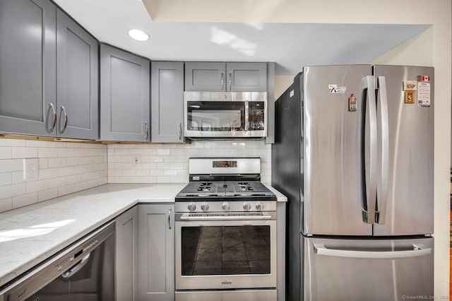 kitchen featuring tasteful backsplash, light stone counters, recessed lighting, gray cabinets, and appliances with stainless steel finishes