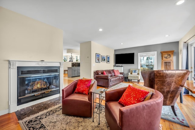 living area featuring a glass covered fireplace, recessed lighting, and wood finished floors