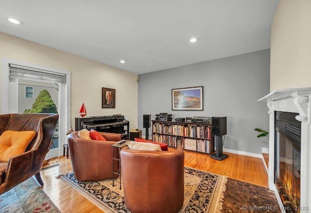 living area with a glass covered fireplace, recessed lighting, wood finished floors, and baseboards