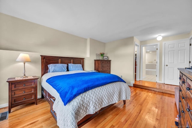 bedroom with connected bathroom, baseboards, visible vents, and light wood-style flooring