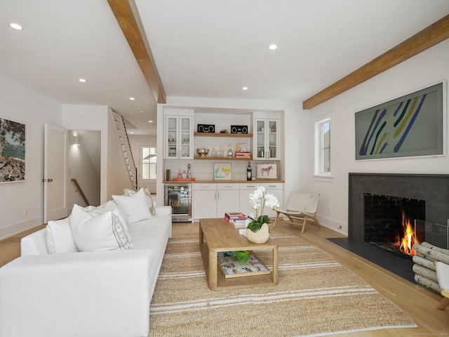 living area with beverage cooler, a fireplace with flush hearth, light wood-style floors, a dry bar, and beamed ceiling