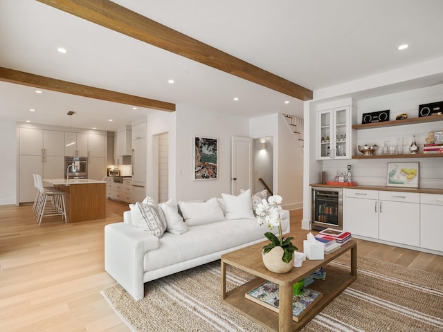 living area with wine cooler, beam ceiling, stairway, light wood-type flooring, and bar