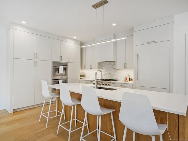 kitchen featuring a breakfast bar area, a sink, appliances with stainless steel finishes, light wood-type flooring, and decorative backsplash