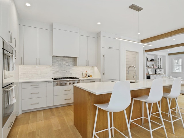 kitchen featuring light wood-style flooring, white cabinets, appliances with stainless steel finishes, modern cabinets, and a kitchen bar