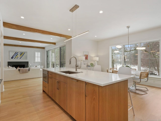 kitchen featuring open floor plan, a kitchen island with sink, a sink, a healthy amount of sunlight, and light wood-type flooring