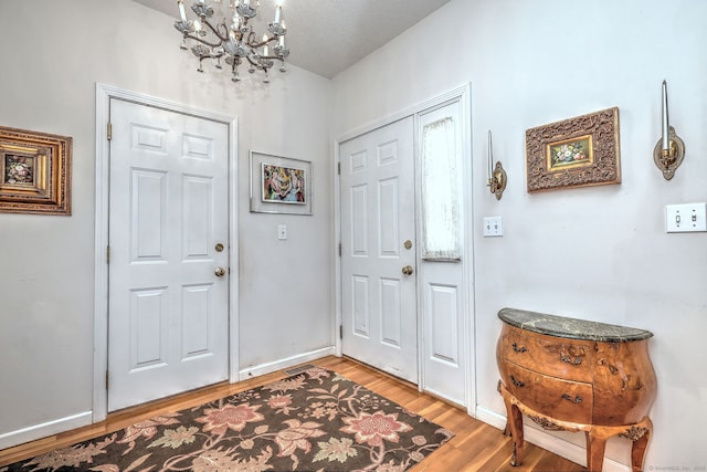 entryway featuring baseboards, light wood-type flooring, and a notable chandelier