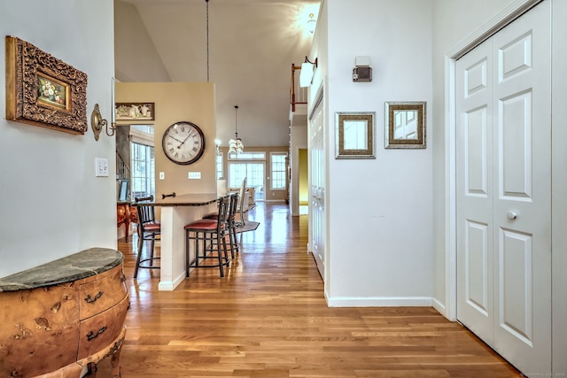 corridor featuring high vaulted ceiling, baseboards, and light wood finished floors