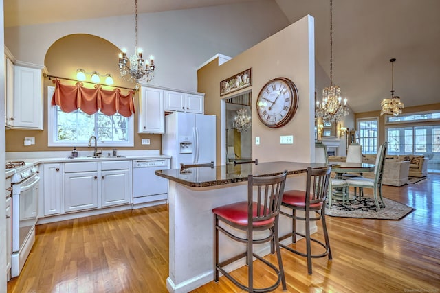 kitchen with white appliances, white cabinets, light wood-style flooring, a chandelier, and a sink