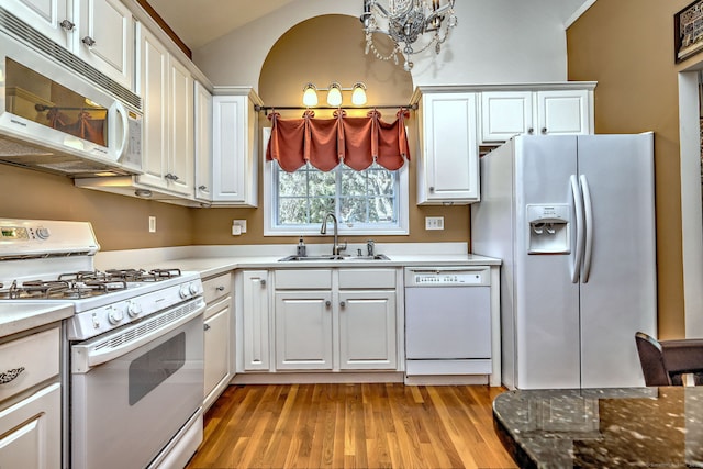 kitchen with lofted ceiling, white appliances, a sink, white cabinets, and light wood-type flooring