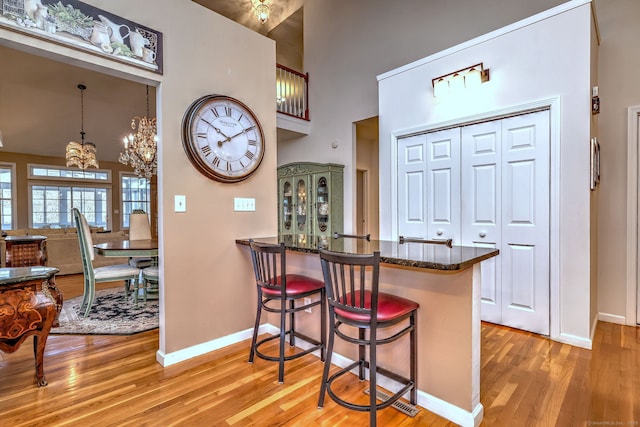 kitchen featuring a towering ceiling, baseboards, light wood-style floors, dark stone countertops, and a kitchen bar