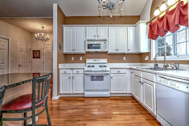 kitchen with white appliances, a notable chandelier, light wood-type flooring, white cabinetry, and a sink