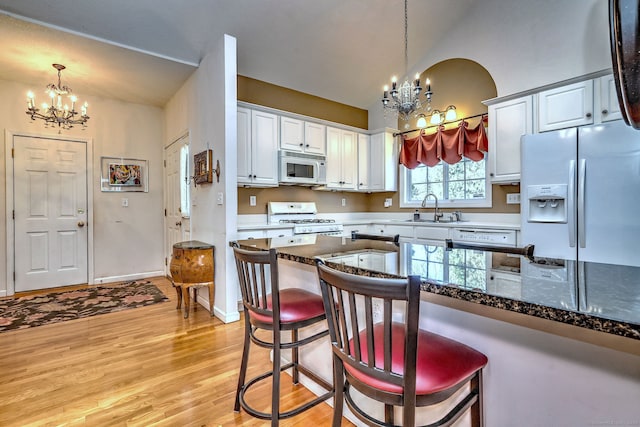 kitchen featuring a notable chandelier, a breakfast bar area, light wood finished floors, a sink, and white appliances