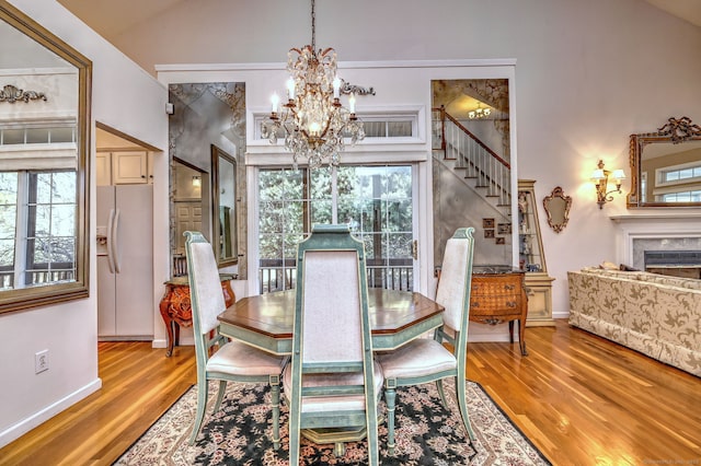 dining area featuring wood finished floors, stairs, vaulted ceiling, a chandelier, and a high end fireplace