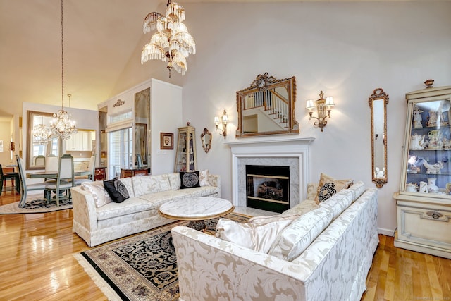 living room with a chandelier, light wood finished floors, a high ceiling, and a high end fireplace